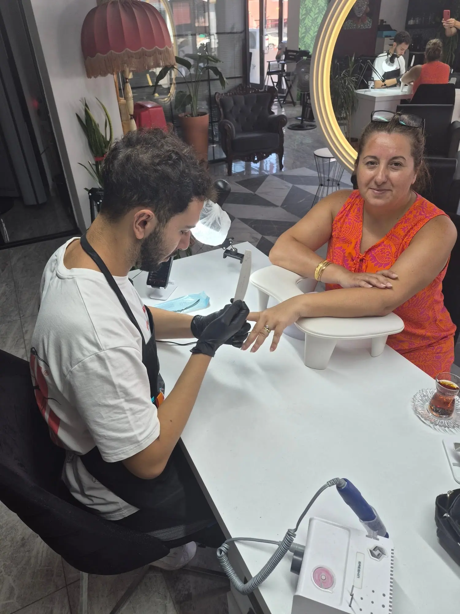 Tırnak masasında manikür uygulaması, arka planda altın ışıklı ayna