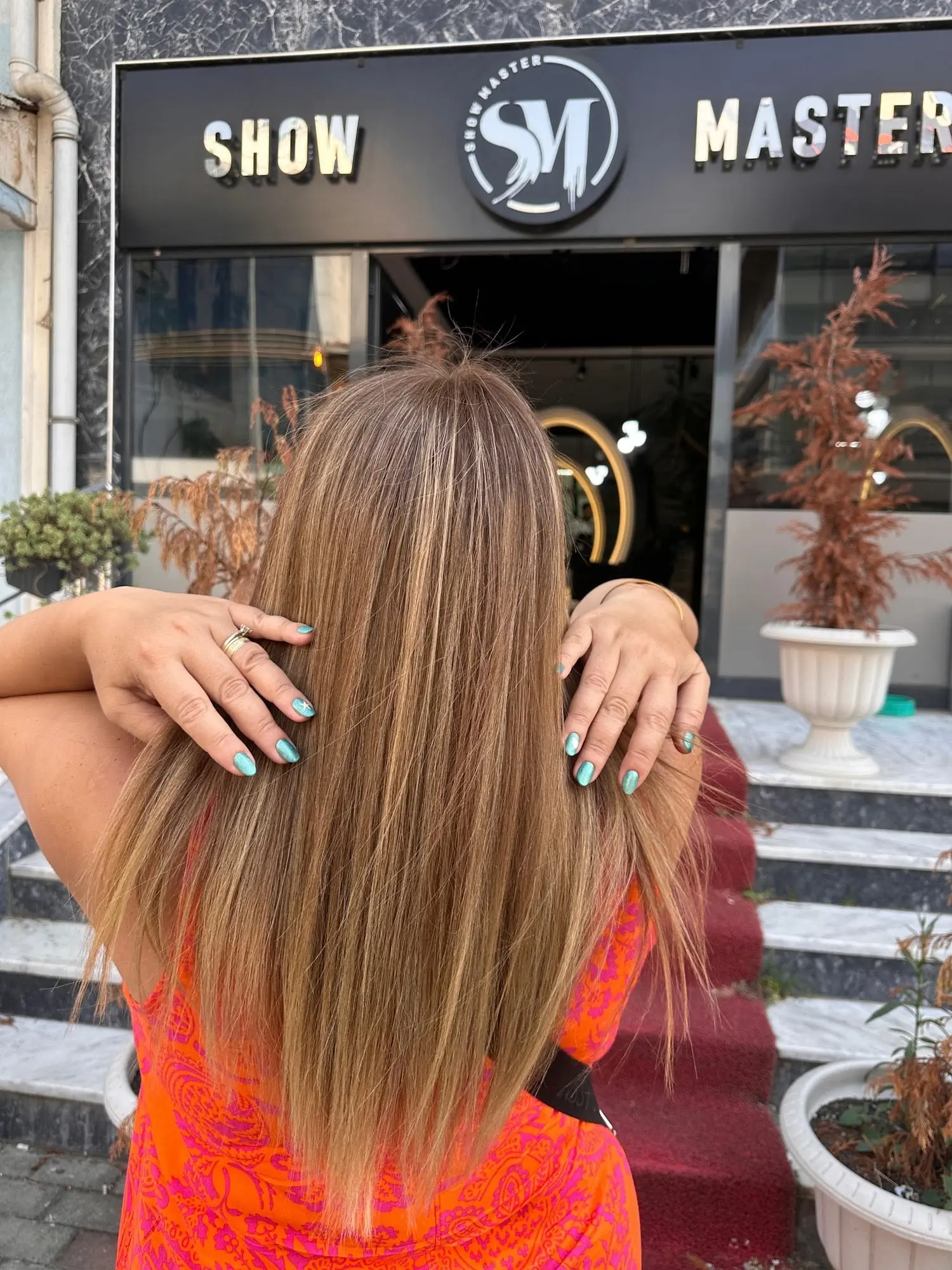 Show Master tabelalı salon girişinin önünde uzun, parlak saçlarını gösteren müşteri